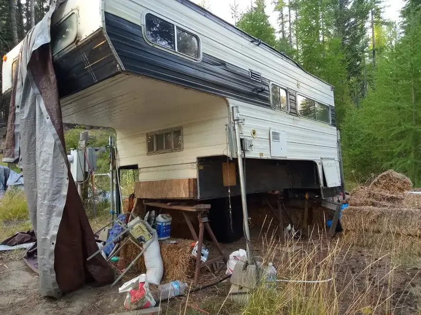 Old slide-in truck camper abandoned in rural area before removal